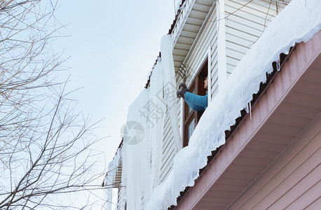 工作一个人从屋顶上搬走巨型冰柱和雪从窗户穿过在农村的季节建筑维护概念中使用干草叉在明冬日用洞叉把大冰柱和雪从窗边移走白色的建造图片