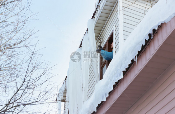 工作一个人从屋顶上搬走巨型冰柱和雪从窗户穿过在农村的季节建筑维护概念中使用干草叉在明冬日用洞叉把大冰柱和雪从窗边移走白色的建造图片