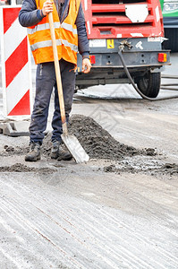 弹幕街道一名身穿橙色背心手拿着铲子的公路工人站在道修理工前面垂直图像象复制空间一名身戴橙色背心的公路工人其背景是修路工作区清理图片