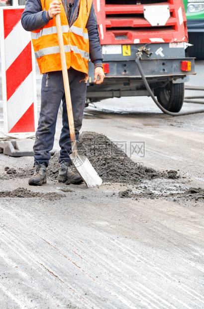 弹幕街道一名身穿橙色背心手拿着铲子的公路工人站在道修理工前面垂直图像象复制空间一名身戴橙色背心的公路工人其背景是修路工作区清理图片