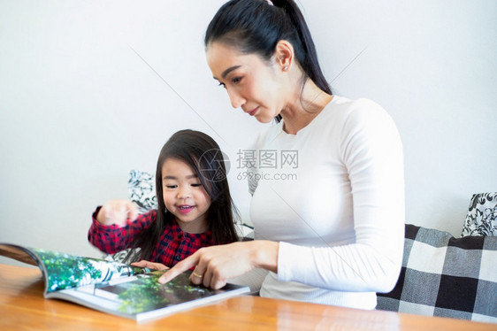 爱室内的一位亚洲母亲正在教她的女儿学期休息间客厅的桌子上看书并在家里的桌子上放冷牛奶家庭的教育理念和活动孩子图片