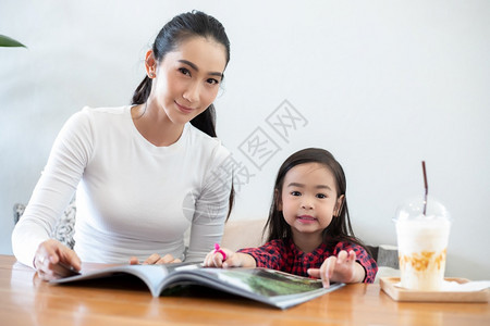 一位亚洲母亲正在教她的女儿学期休息间客厅的桌子上看书并在家里的桌子上放冷牛奶家庭的教育理念和活动姐母粘合图片