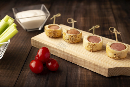 包着切片香肠的美味零食和加芝麻种子的松糕饼配有樱桃番茄大菜棒和酱汁的芝麻籽放在木板上熟食劳斯莱派对图片