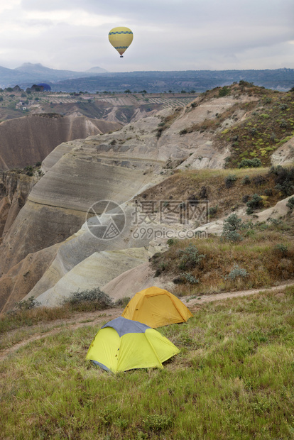 无雪火山云游客帐篷位于山顶上一座其背景是一辆气球在卡帕多西亚的红谷旅游帐篷中飞过红谷上空还有一条小路上的气球面有红色谷风景辉煌的图片