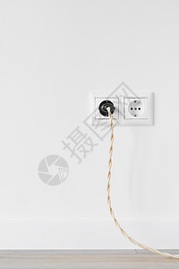 在白石膏墙上隔离的欧洲新白色塑料电源插口装有老旧电缆的插塞在玻璃木地板的喷口间隙中家电的塞住图片