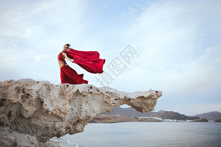 身穿红礼服的黑发年轻女人在海滨附近岩石上跳舞水平的独自女图片