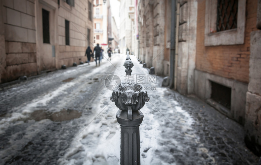近距离观看一个装饰着交通覆盖的圆柱子在城市小巷中被雪封在一栋城胡同里人们在幕后行走外部的过去城市图片