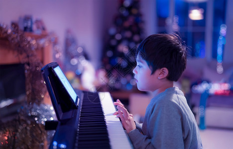 娱乐爱好孩子用霓虹灯弹钢琴的电影夜间肖像小男孩在客厅用电钢琴学习音乐孩子在圣诞节晚上家轻松地唱歌练习图片