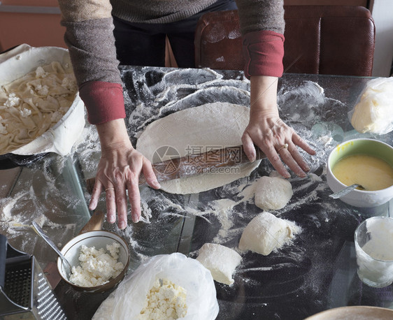 女人双手在玻璃桌上卷着面团做蛋糕干芝士面包馅饼加卷心菜揉白色的制作图片