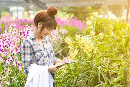 快乐的研究员植物兰花身戴白帽子手拿着笔和记本作研究录户外新鲜的绿色图片