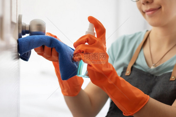 穿着橙色橡胶手套的有吸引力亚洲妇女用橘色橡皮手套擦门把在房子里喷上酒精清洗雾剂对卫生进行排污美丽笑容的家庭主妇和务工作Coron图片