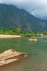 亚洲人皮艇旅游清晨南宋江的风景欧洲游客在河上划艇老挝男孩横跨悬吊桥VangVieng老挝关注地表急速图片