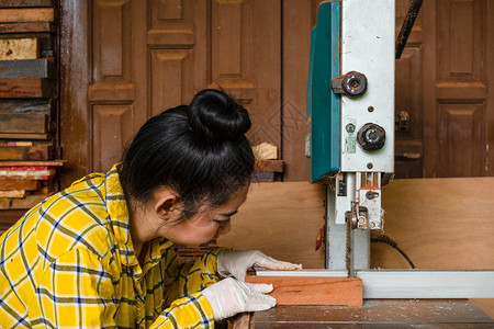 木制的锯末站立妇女正在工作板上用木车间匠机的带锯子发电工具在作台上手艺切割木材人锯板从工人那里经营一家庭企业美丽的图片