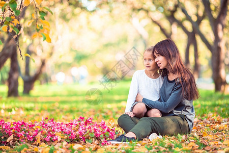 树落下乐趣年轻妈和可爱小女孩在阳光明日的秋天公园有可爱小女孩在秋天的公园家庭在清晨享受温暖的天气小女儿和妈在秋天公园户外图片