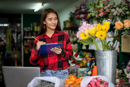 植物无线的亚洲女花粉小商鲜店老板和持有剪贴纸写作为她的商店订单工作愉快背景图片
