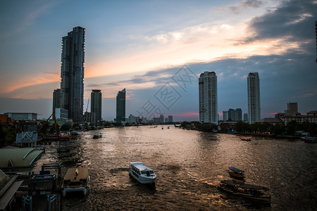 海滨泰国曼谷河岸一带船只和现代建筑的景象ChaoPhraya河日落风景泰国曼谷现代的鸟类图片