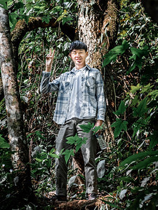 年轻有背包架的亚洲男子与背包站立的年轻男子在度假旅行时休息被森林中老树大美人拍下的照片环境茶点经过图片