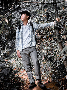 亚洲人户外年轻有背包架的亚洲男子与背包站立的年轻男子在度假旅行时休息被森林中老树大美人拍下的照片经过图片