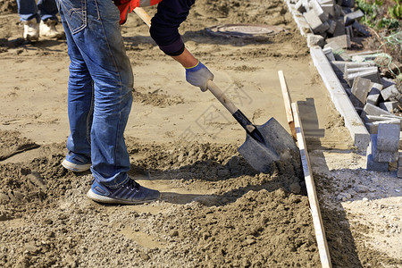 砂浆乌克兰摊铺机工人将地基与沙子和木制层下的铲子对齐以在为工作人员准备的地背景上铺筑路板用木制层的铲子土砂平整地基图片
