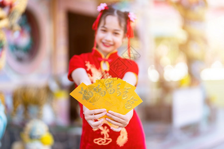 奖金穿着青山红传统装饰重点节目的亚洲可爱小女孩手拿着黄色信封在中华神庙举办新年庆典节日活动美丽旗袍图片