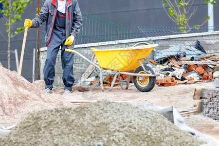 递送基础在建筑工作场所的背景下一名身穿蓝衣的工人站在沙堆和一辆黄色的建筑轮车旁边一个建筑工作场所的背景是工人用复制版空间图像在沙图片