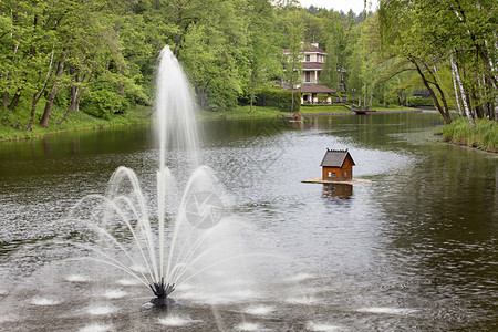 古朴在池塘中心一个舒适的不老泉咖啡馆和图片公园中漂浮鸭屋的背景下一个光滑的春天公园有一个大而宽阔的池塘中间有喷泉还两座悬浮的鸭子图片