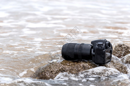 在极端环境旅行和试验时摄影师DSL用DSR相机在海浪的石滩上用探水器湿透了海浪的石滩上摄像头破碎的孤独信号图片