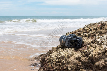 现代的在极端环境旅行和试验时摄影师DSL用DSR相机在海浪的石滩上用探水器湿透了海浪的石滩上摄像头海洋假期图片