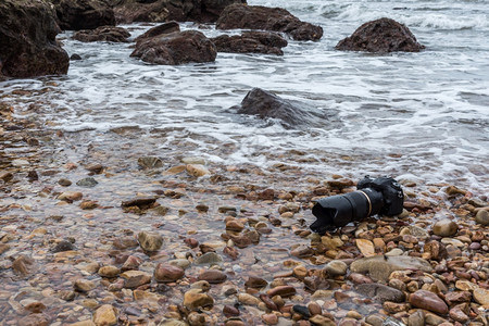浸泡在极端环境旅行和试验时摄影师DSL用DSR相机在海浪的石滩上用探水器湿透了海浪的石滩上摄像头信号技术图片