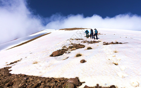 他们的团体一群背着包的游客在岩石积雪覆盖的斜坡上徒步旅行到达土耳其Erciyes山的云雾之巅一群游客爬上岩石积雪覆盖的山坡到达雾图片