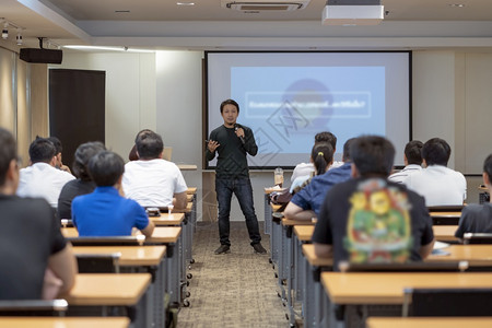 研究所亚洲演讲人在会议室前的舞台上临时穿着便衣在商业或教育研讨会商业和教育概念的演示屏幕上低亮地播放讲演者商业和教育概念讲台观众背景图片