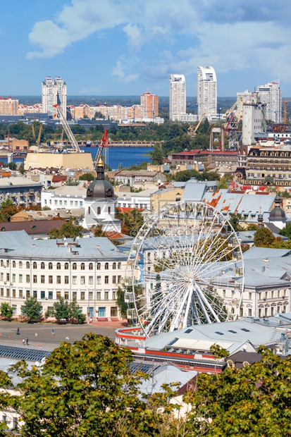钟行业古老的Podil夏季基辅Ferris轮稠密的住宅建筑和地平线垂直图像上的新邻居景象以旧Podil区为例用Ferris车轮旅图片