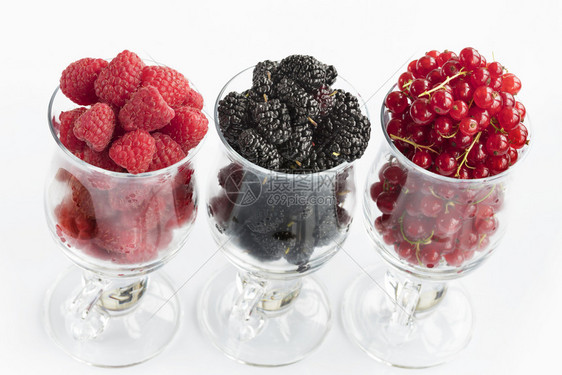 站立成熟黑莓大和红沙律被倒入透明的拿铁杯中在光背景上排成一高键Raspberry的图像大黑莓和红草原以光背景置于清晰的玻璃里一个图片