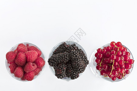 站立果味黑莓大和红沙律被倒入透明的拿铁杯中在光背景上排成一高键Raspberry的图像大黑莓和红草原以光背景置于清晰的玻璃里一个图片
