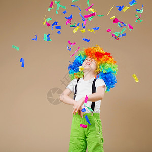 笑声快乐的小丑男孩大彩色假发Lensrcopos党白日概念一个孩子的肖像扔出一个多色的锡子和涂面生日男孩浮夸噱头图片