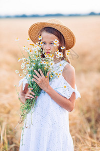 黑麦场地关心有趣的快乐女孩在小麦田中玩得开心一束香米花放在小麦田的手中快乐孩子在小麦田中幸福快乐美丽的女孩穿着白色衣服戴草帽手拿图片