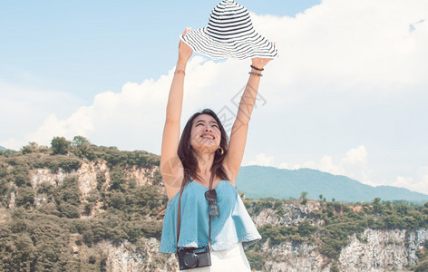 独自的穿戴帽子和拉起手的漂亮美丽亚洲妇女在夏季旅行时身着高山和蓝天的模糊背景潮人女士图片