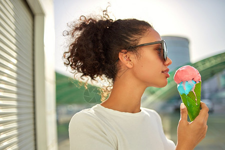 穿着白色T恤衫和轻牛仔裤的年美籍非裔女孩在阳光日吃冰淇淋有选择地关注小重点领域夏天晴非裔美国人图片