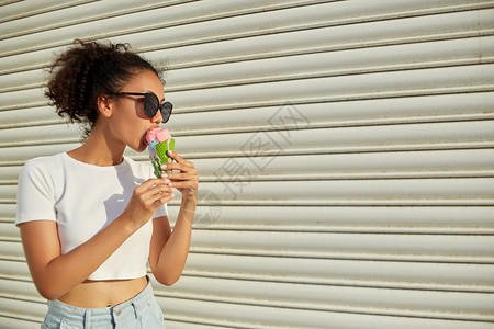 女穿着白色T恤和轻牛仔裤的年美籍黑人女孩在日光照耀时用冰淇淋抵挡着一堵轻墙吃冰淇淋美丽的非洲人图片