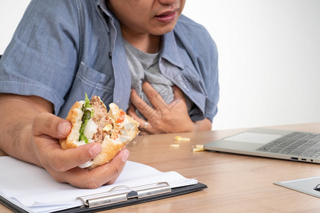 早餐笔记本电脑桌子亚洲男在办公桌上工作和吃汉堡心脏病和发作一个繁忙的商人概念不能工作左平衡不能照顾健康只吃垃圾食品只能吃垃圾食品图片