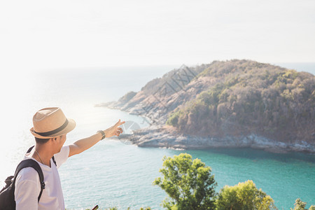 闲暇身戴帽子的人手握着他快乐的ManAsiian旅游者看着山峰和海在日落前的活动生方式在户外自由或旅行游激励背包客到19岁混合灵图片