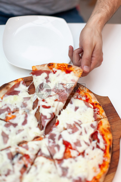 脆的咖啡店比萨男人抢了第一块美味的意大利比萨饼手架拿了一块热披萨火腿在木板上白餐桌配着盘子图片