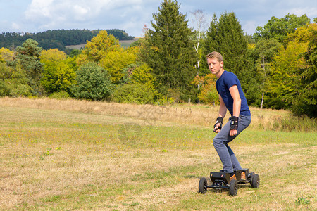 景观年轻的高加索人骑着自然的离路电动山坡荷兰语滑板图片