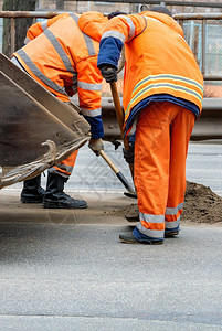 构造一队穿着亮橙色反光制服的道路工人正在清理一段道路复制空间垂直图像一队道路工人使用铲子清理一段道路垂直图像打扫铺沥青图片