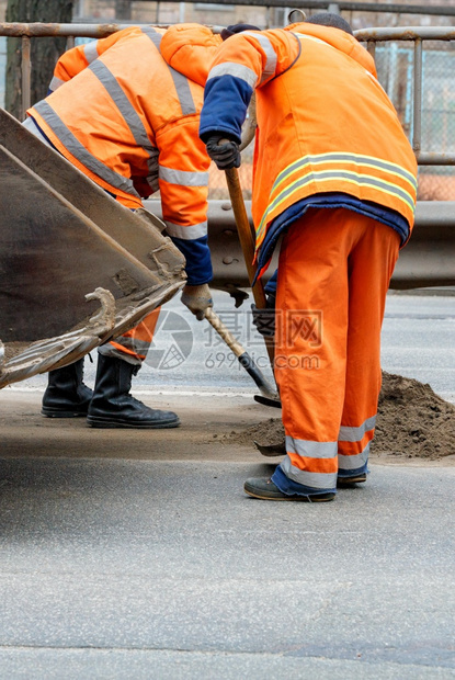 构造一队穿着亮橙色反光制服的道路工人正在清理一段道路复制空间垂直图像一队道路工人使用铲子清理一段道路垂直图像打扫铺沥青图片