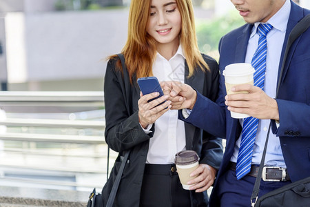 商业女人在镇上喝咖啡办公室外使用智能手机现代城市举起来抢走咖啡杯和智能电话与商业伙伴一起用咖啡谈生意伙伴的心话咖啡店行政人员工作图片