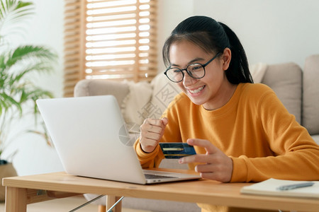 清晨坐在客厅里时美女正在网上用信卡买东西妇女们在使用电脑笔记本在家里进行线交易面对的女孩前笑一种女士商业图片