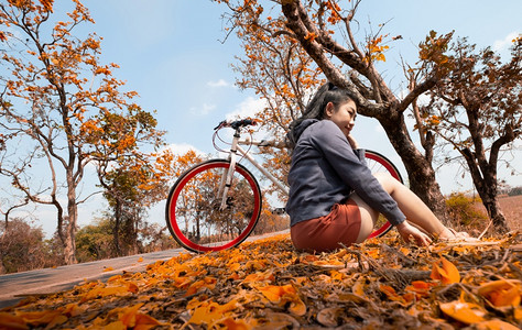 活动美丽的年青轻女子坐在她骑自行车的户外露天在棕榈树边上布提亚莫诺斯珀玛ButeaMonosperma和来自然的东南部布提亚罗多图片