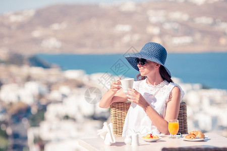 享受欧洲戴帽子的年轻女在户外咖啡馆喝欣赏米科诺斯镇的美景年轻女子在户外咖啡馆喝欣赏米科诺斯镇的美景健康图片