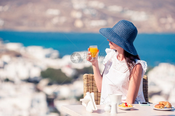 戴帽子的年轻女在户外咖啡馆喝欣赏米科诺斯镇的美景年轻女子在户外咖啡馆喝欣赏米科诺斯镇的美景快乐白色美味图片